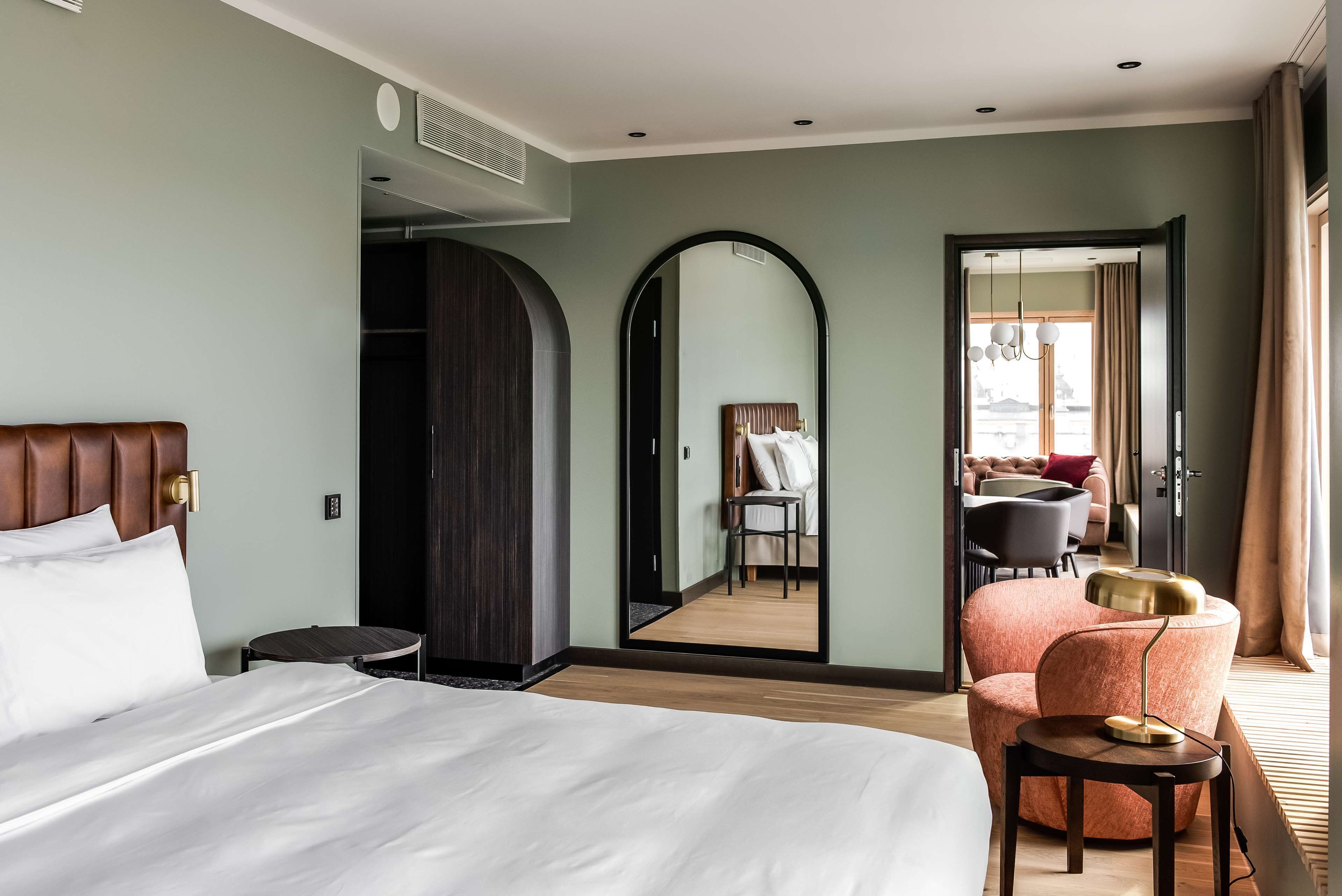 Hotelkamer met een groot bed, een ronde tafel, een stoel, een spiegel en uitzicht buiten door een deur.