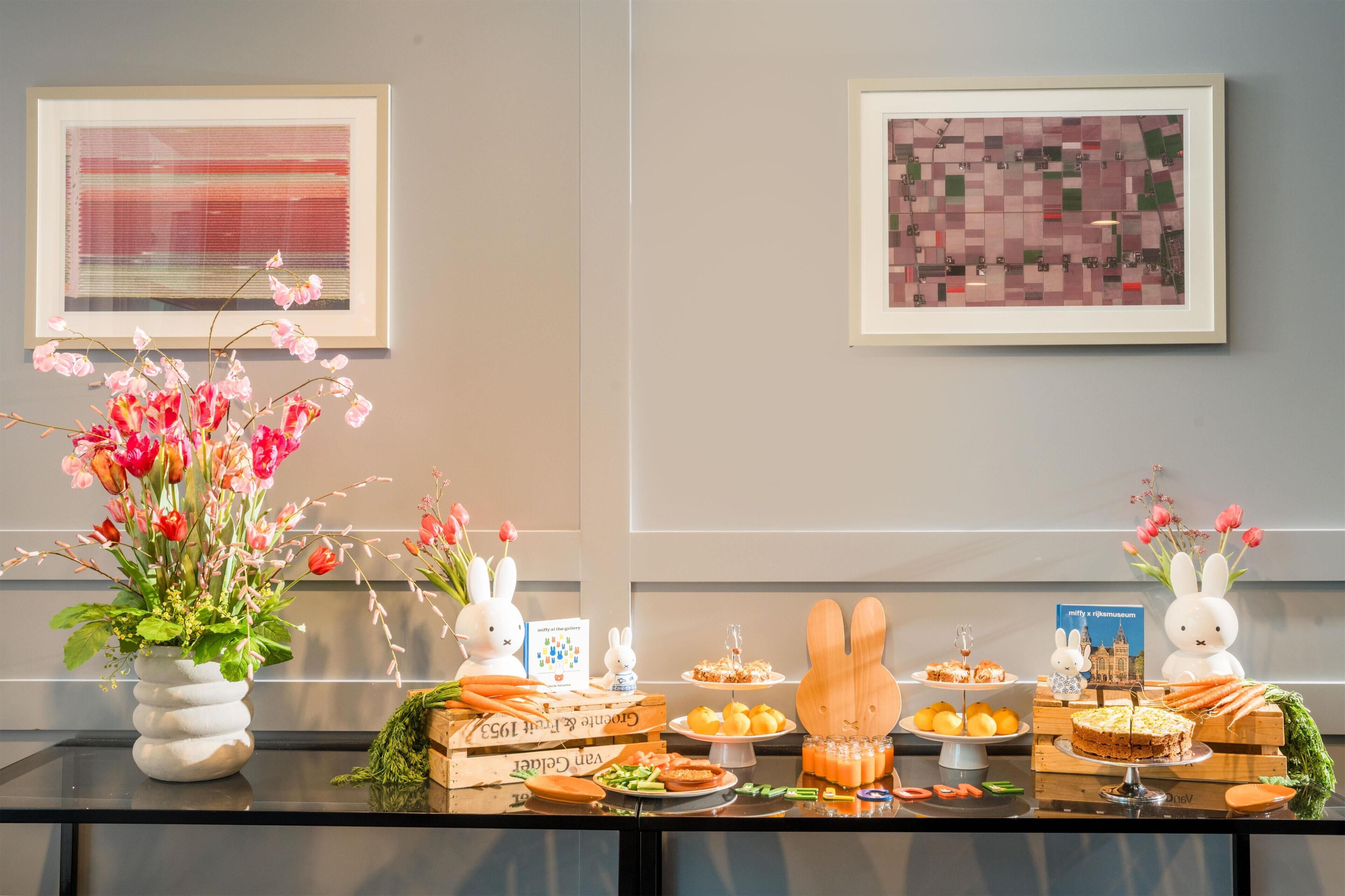 Une table de buffet garnie de plats, un vase rempli de fleurs et des œuvres d’art encadrées accrochées au mur.