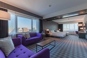 A hotel room with a large bed, a sofa, a desk, and a view of the city.