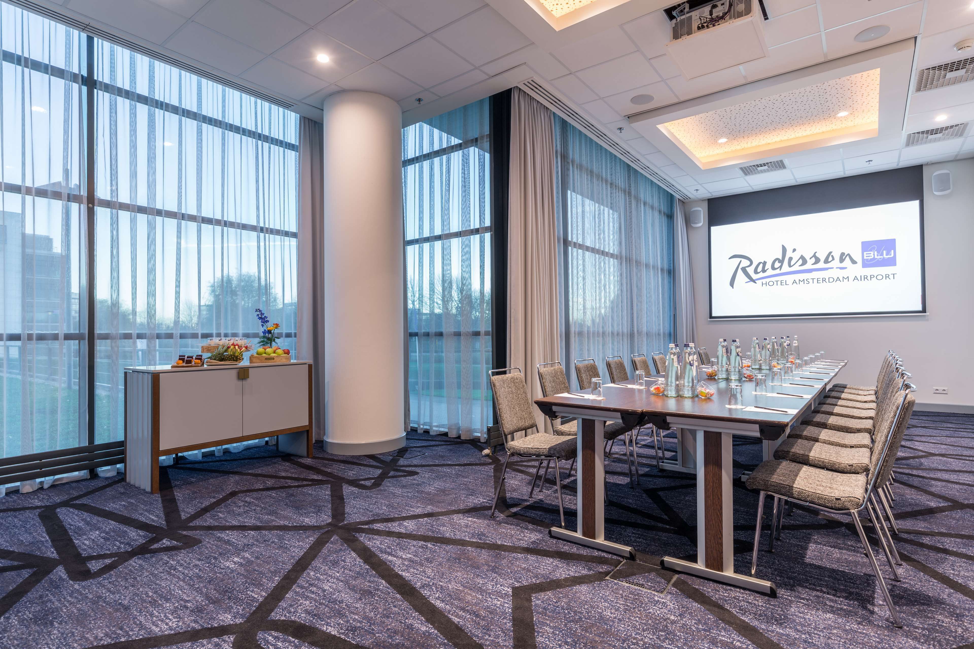 A conference room with a long table, chairs, a projector screen, and large windows.