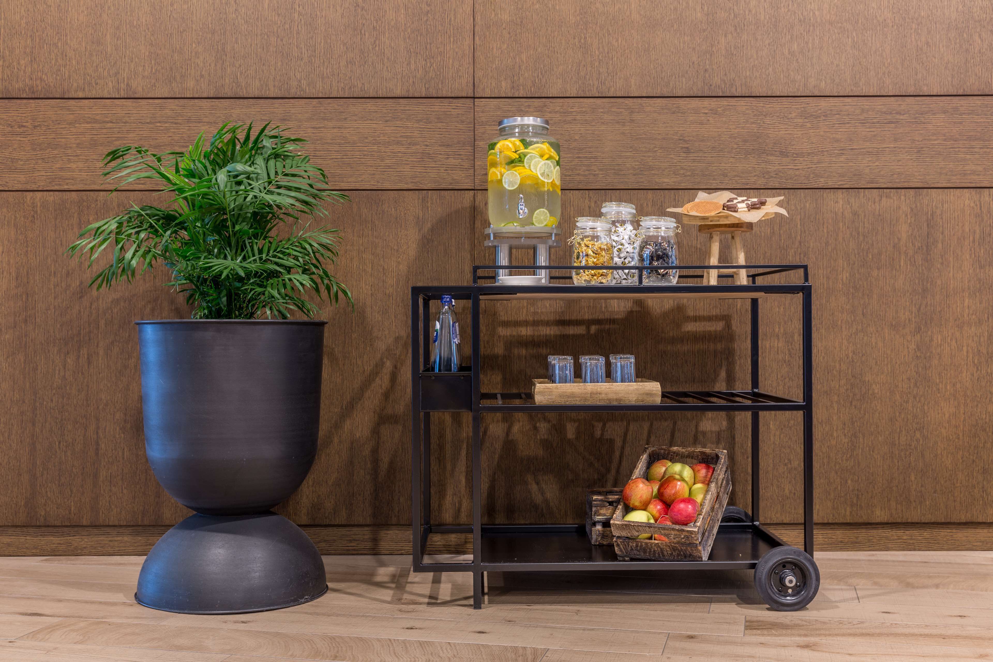 Een zwarte metalen kar met een plant, een grote limonadekan en een houten kist vol appels.