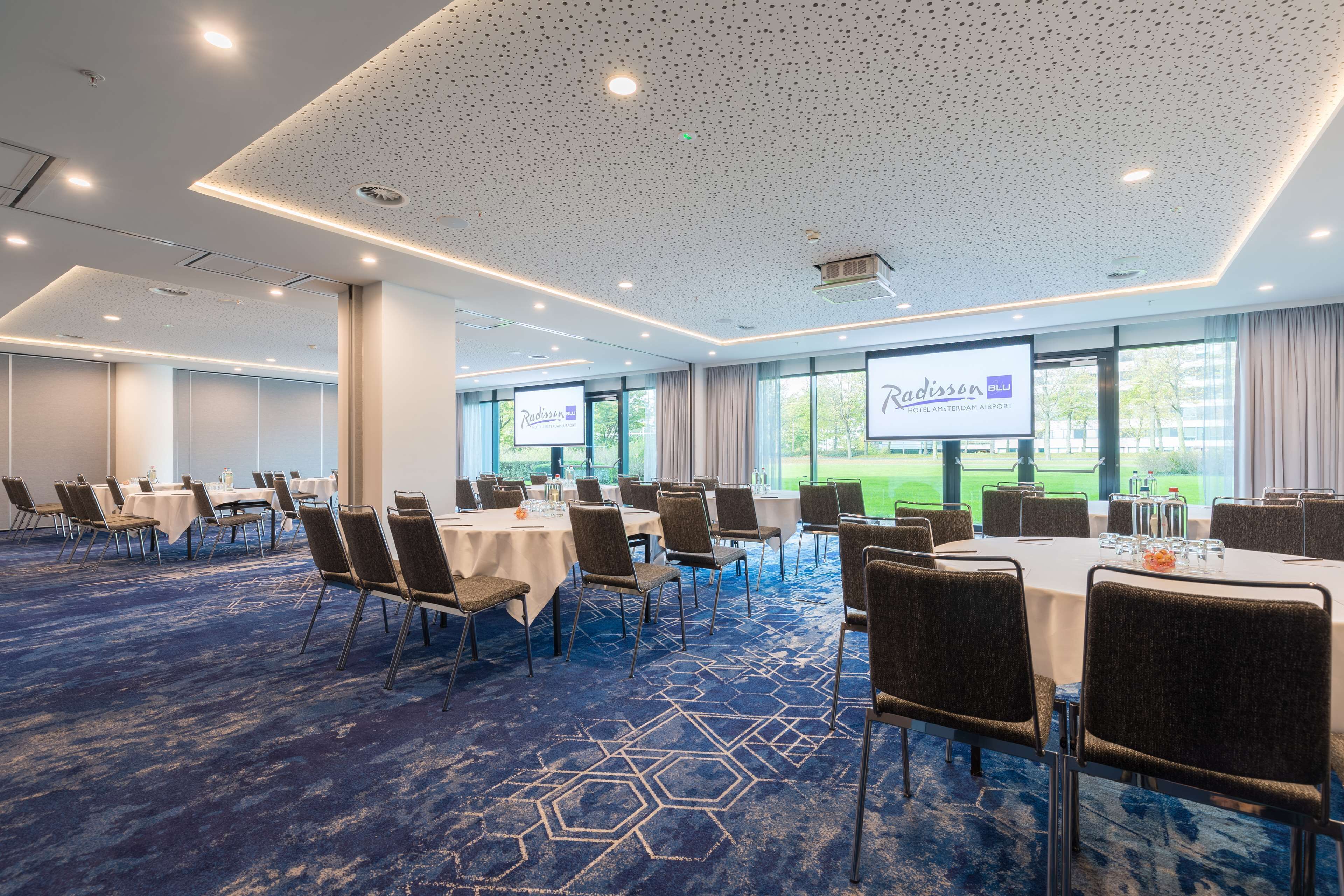 A conference room with tables and chairs, a projector screen, and large windows.