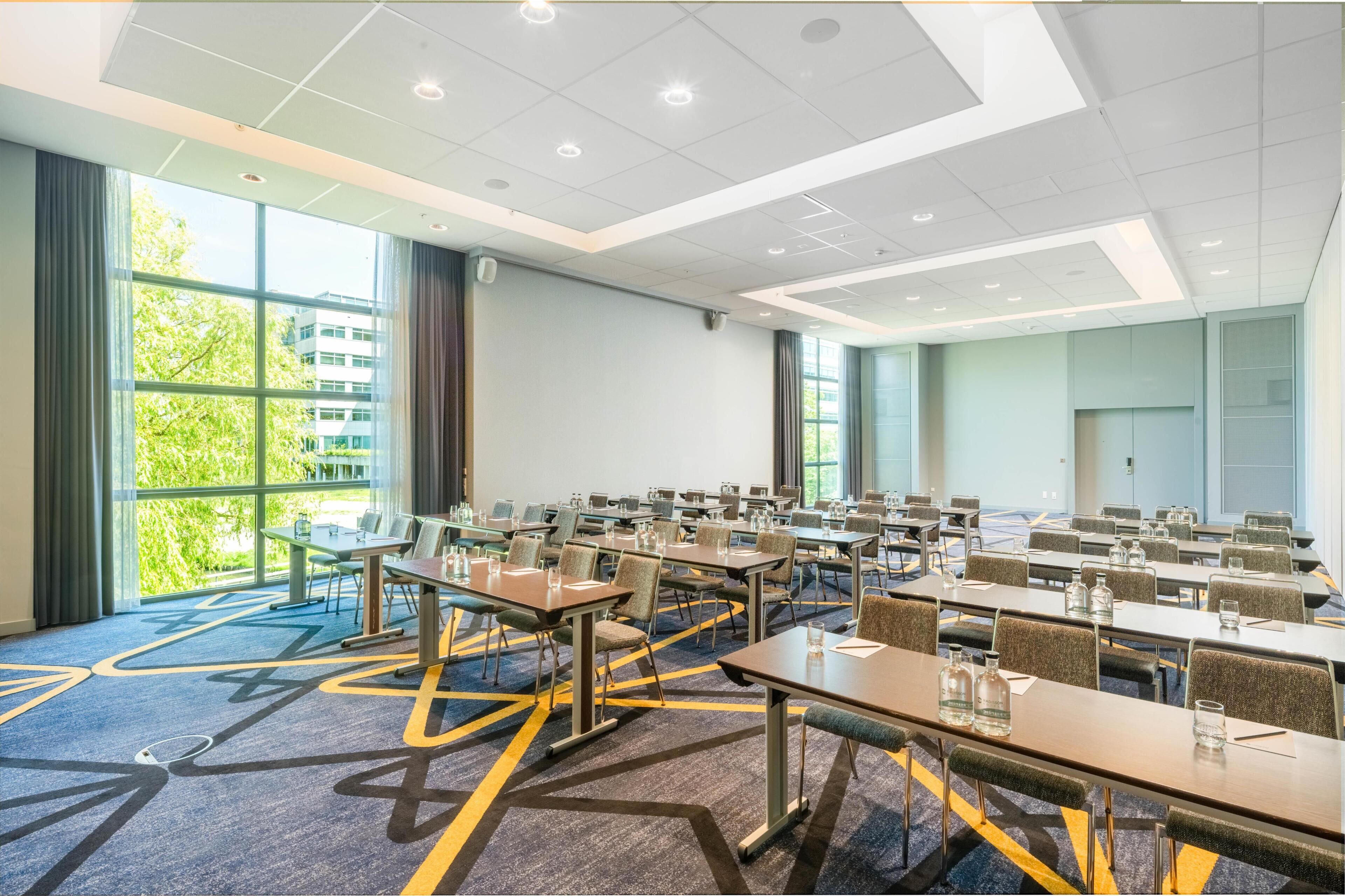 Un salón de conferencias con mesas, sillas y ventanas amplias.