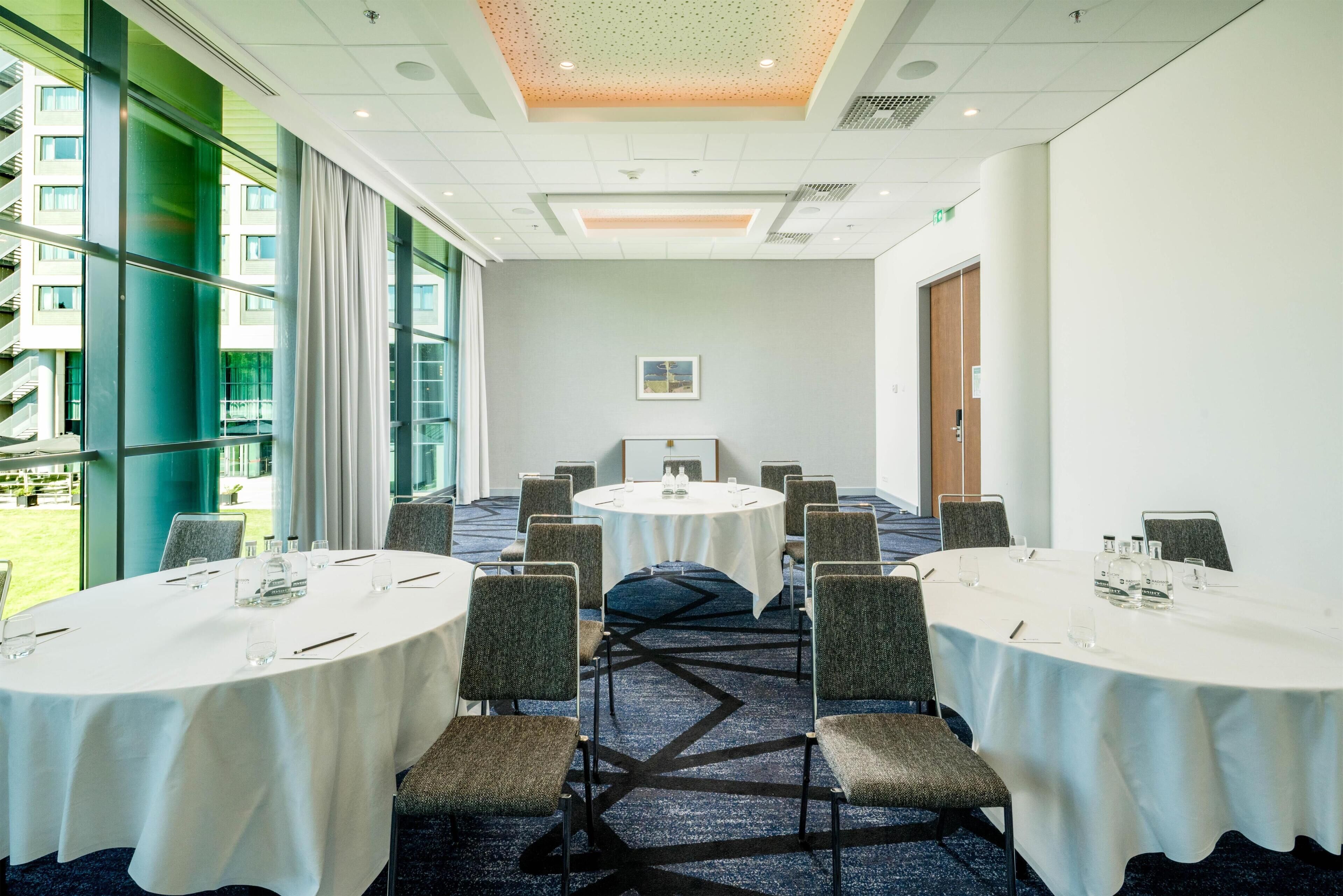 A conference room with round tables, chairs, and a view of a building outside.