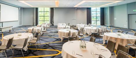 A conference room with multiple round tables, chairs, and a projector screen.