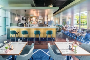 Un moderno vestíbulo de hotel con zona de bar, asientos y ventanas amplias.