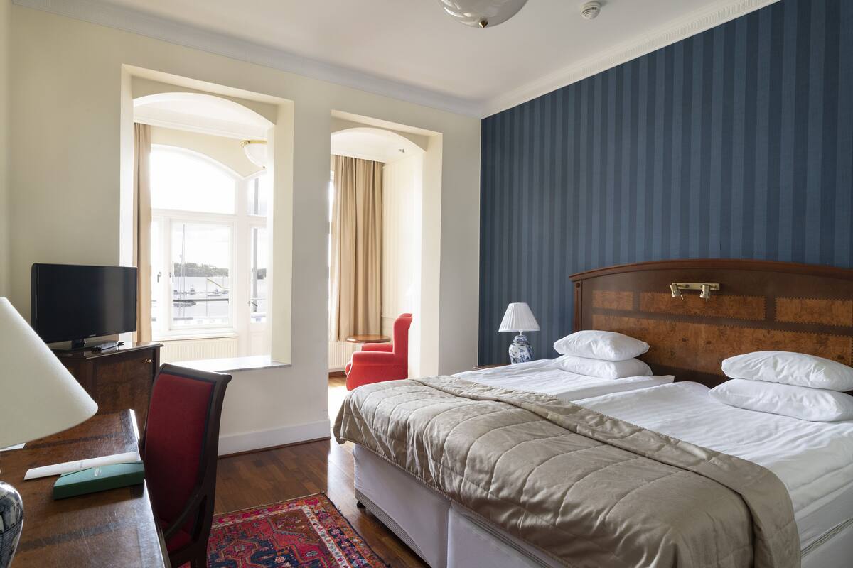 Ein Hotelzimmer mit einem großen Bett, einem Schreibtisch mit Computer, einem Fernseher und einem roten Sessel.