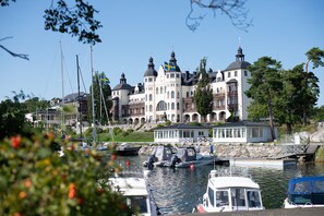 A large, historic building with multiple domes and flags, situated by a body of water with boats docked nearby. - Grand Hotel Saltsjöbaden (Saltsjobaden)