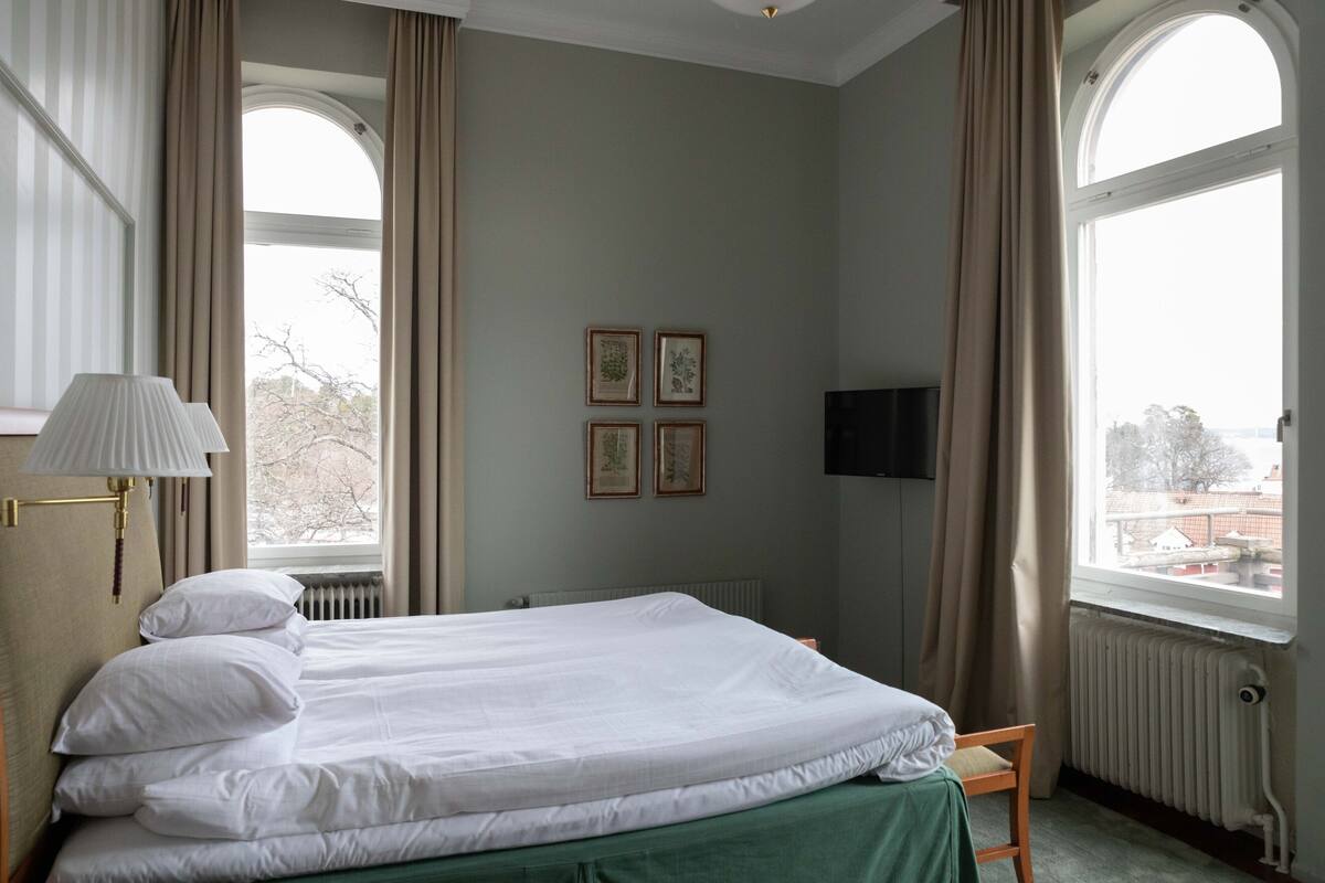 Ein Hotelzimmer mit einem Bett, einem Sessel, einem Fernseher und gerahmten Bildern an der Wand.