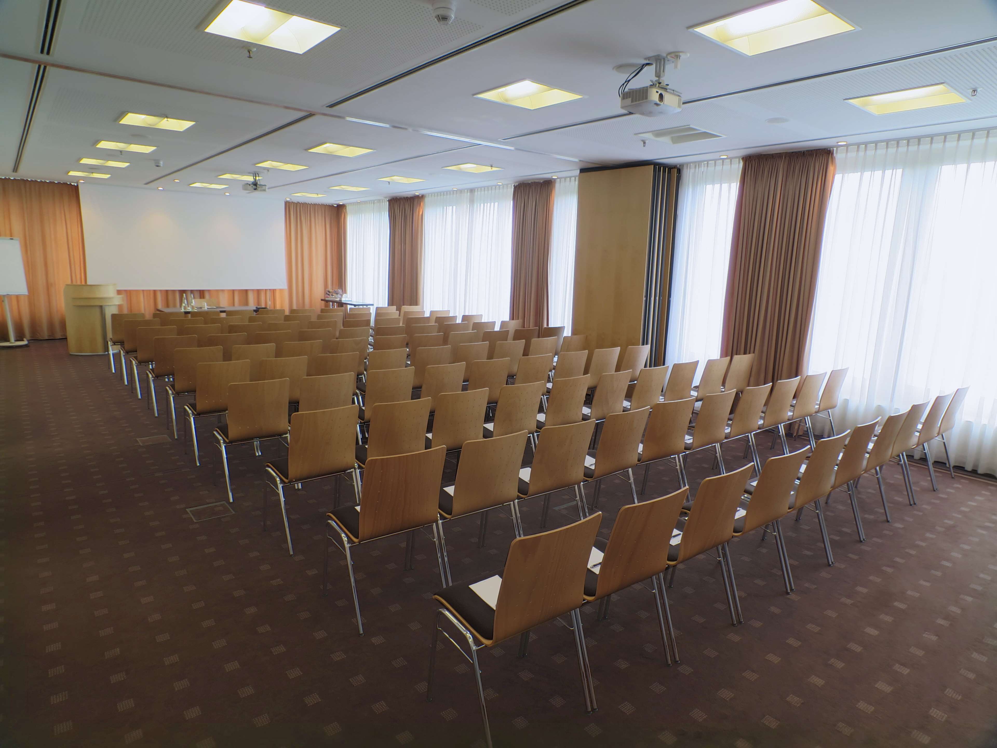 A conference room with rows of chairs, a podium, and large windows with curtains.