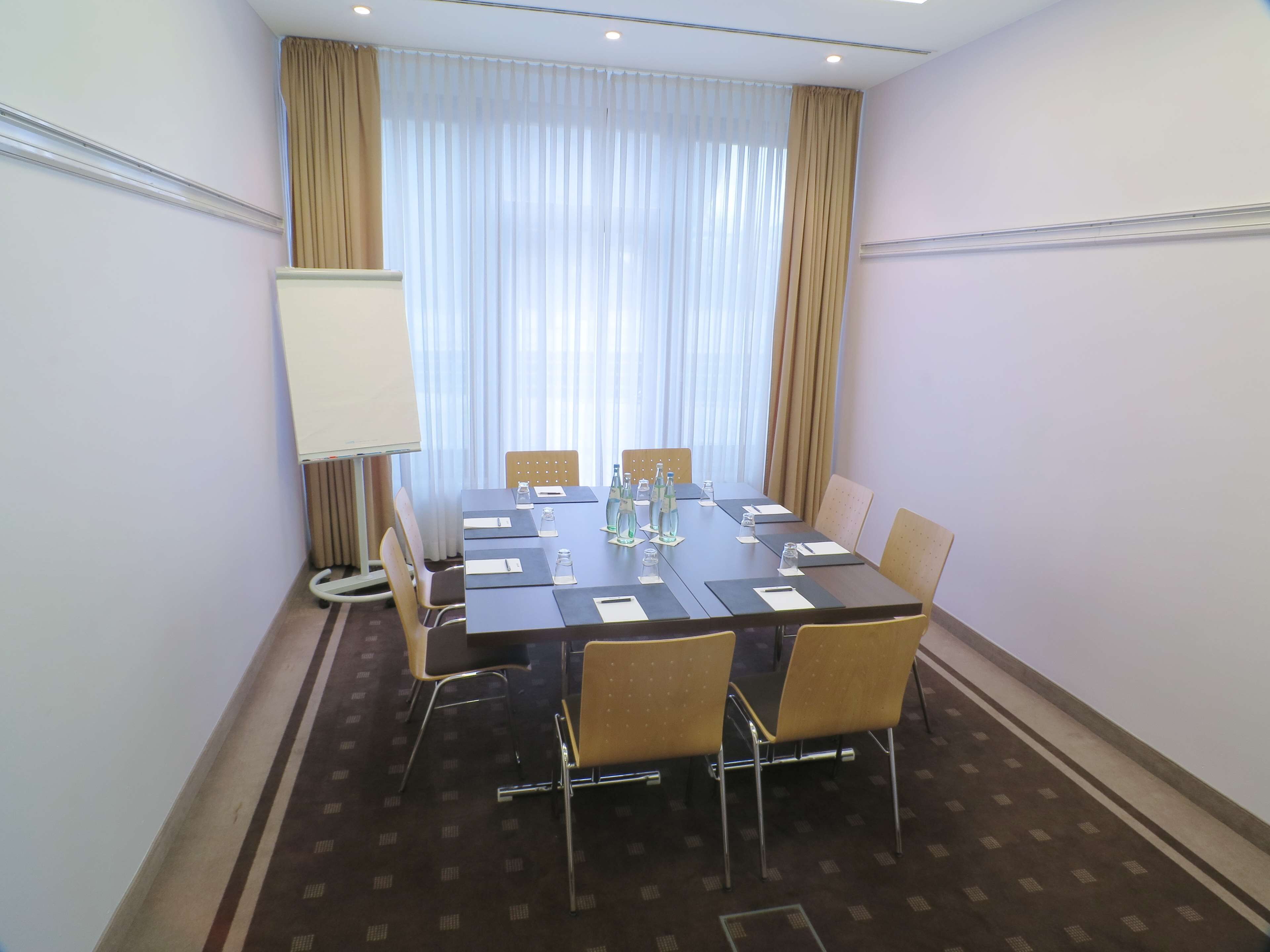 Un salón de conferencias con una larga mesa, sillas, una pizarra y una ventana con cortinas.