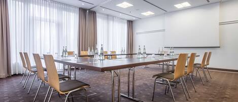 A conference room with a long table, chairs, and a projector screen.