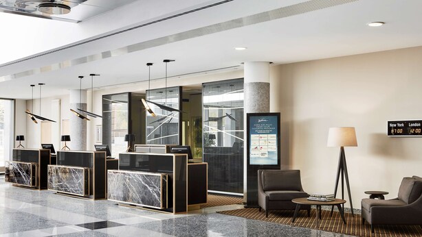 Un moderno vestíbulo de hotel con mostrador de recepción, zona de estar y un reloj digital que muestra información de vuelos.