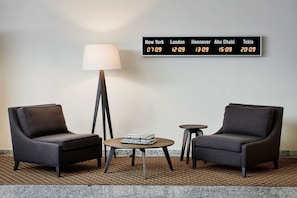 Una habitación de hotel moderna con dos sillones, una mesita, una lámpara y un reloj digital que muestra la hora en varias ciudades.
