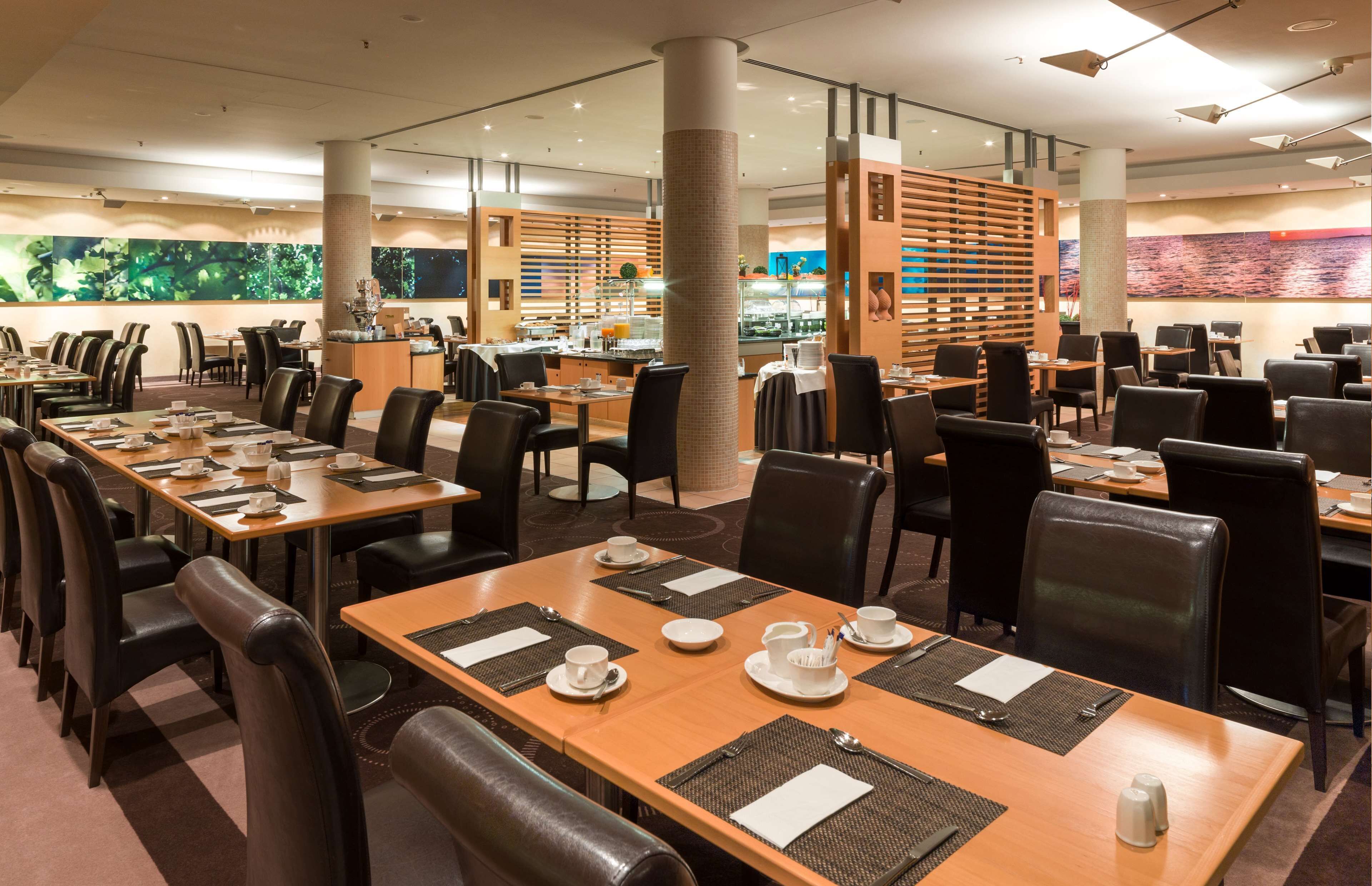 Un ristorante spazioso con numerosi tavoli e sedie, un pilastro centrale e un'area buffet sullo sfondo.