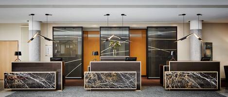 A reception area with a modern design, featuring a reception desk, three marble-patterned consoles, and a large plant.