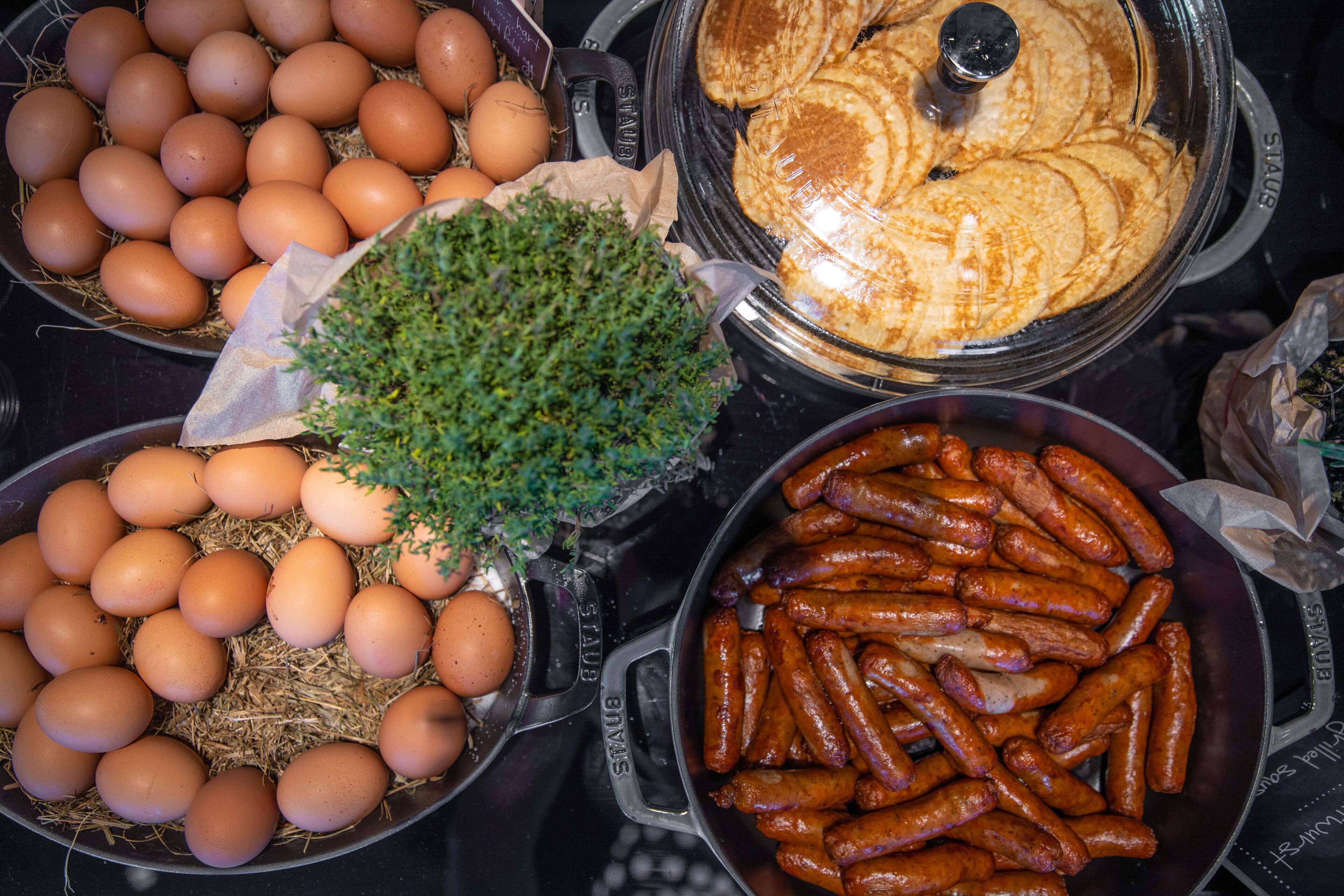 A variety of food items including eggs, sausages, and pancakes in separate containers.