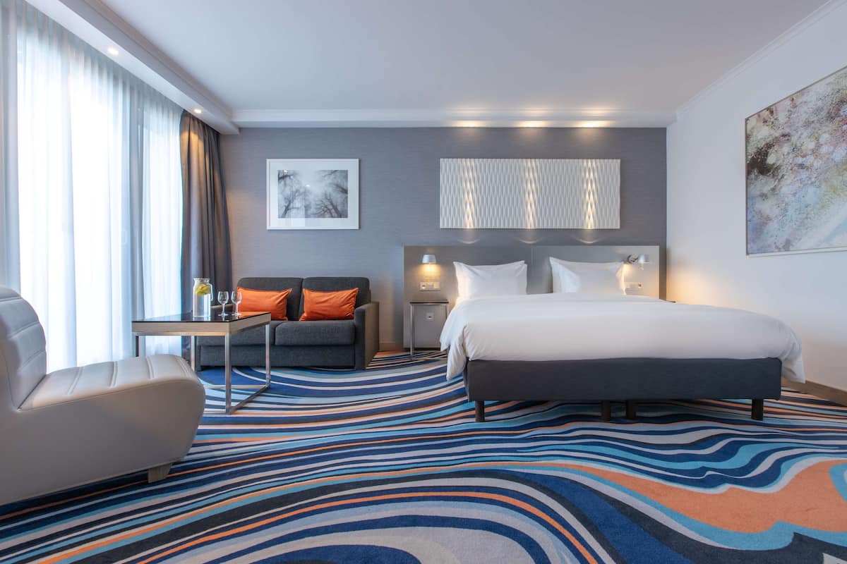 A hotel room with a large bed, a sofa, a desk, and a view of the outdoors.
