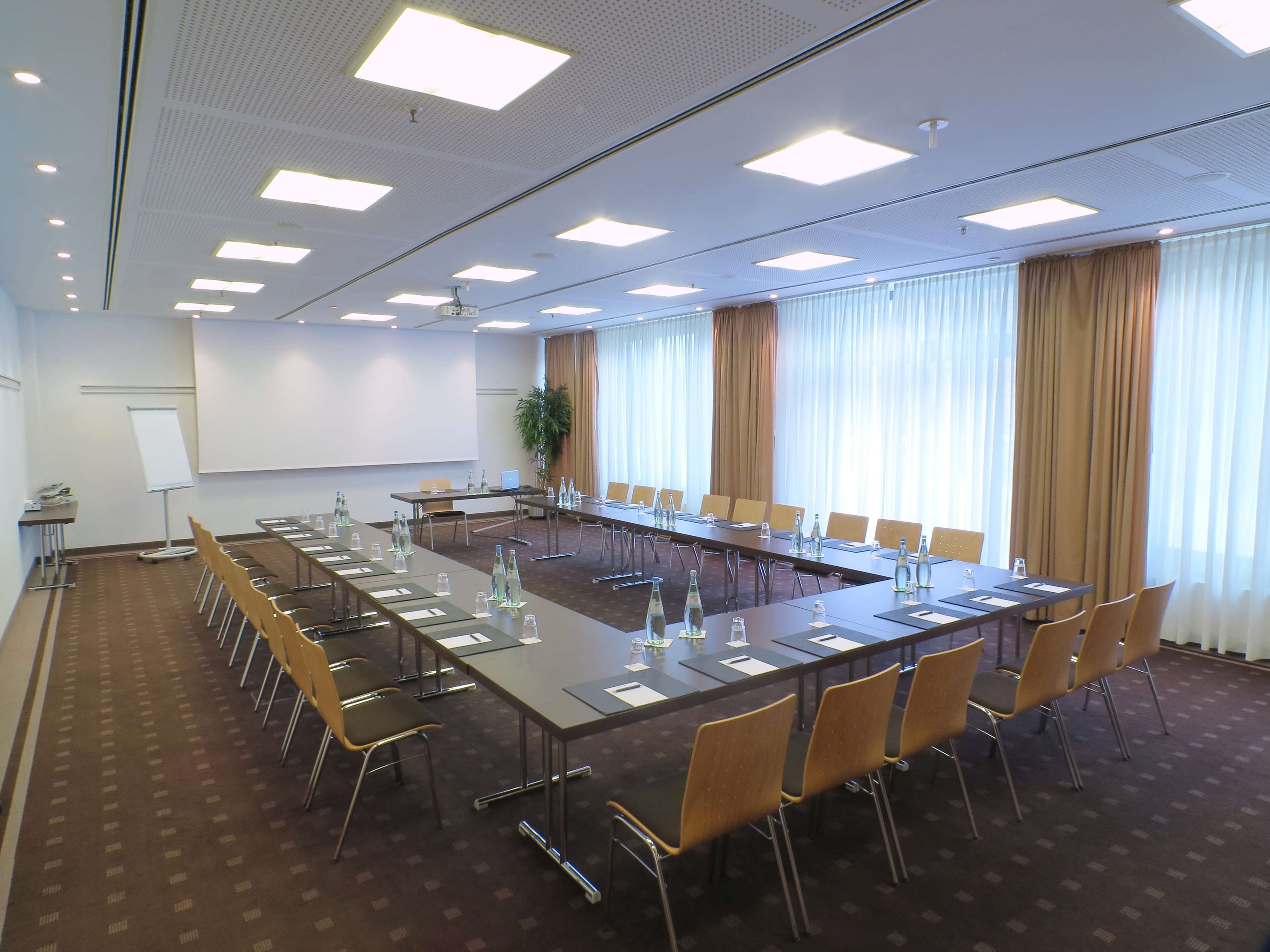 Una sala de conferencias con una larga mesa, sillas, una pantalla de proyector y una pizarra.