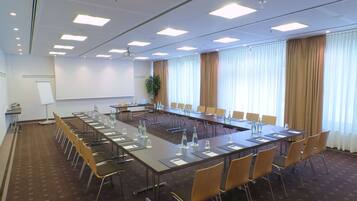 Una sala de conferencias con una larga mesa, sillas, una pantalla de proyector y una pizarra.