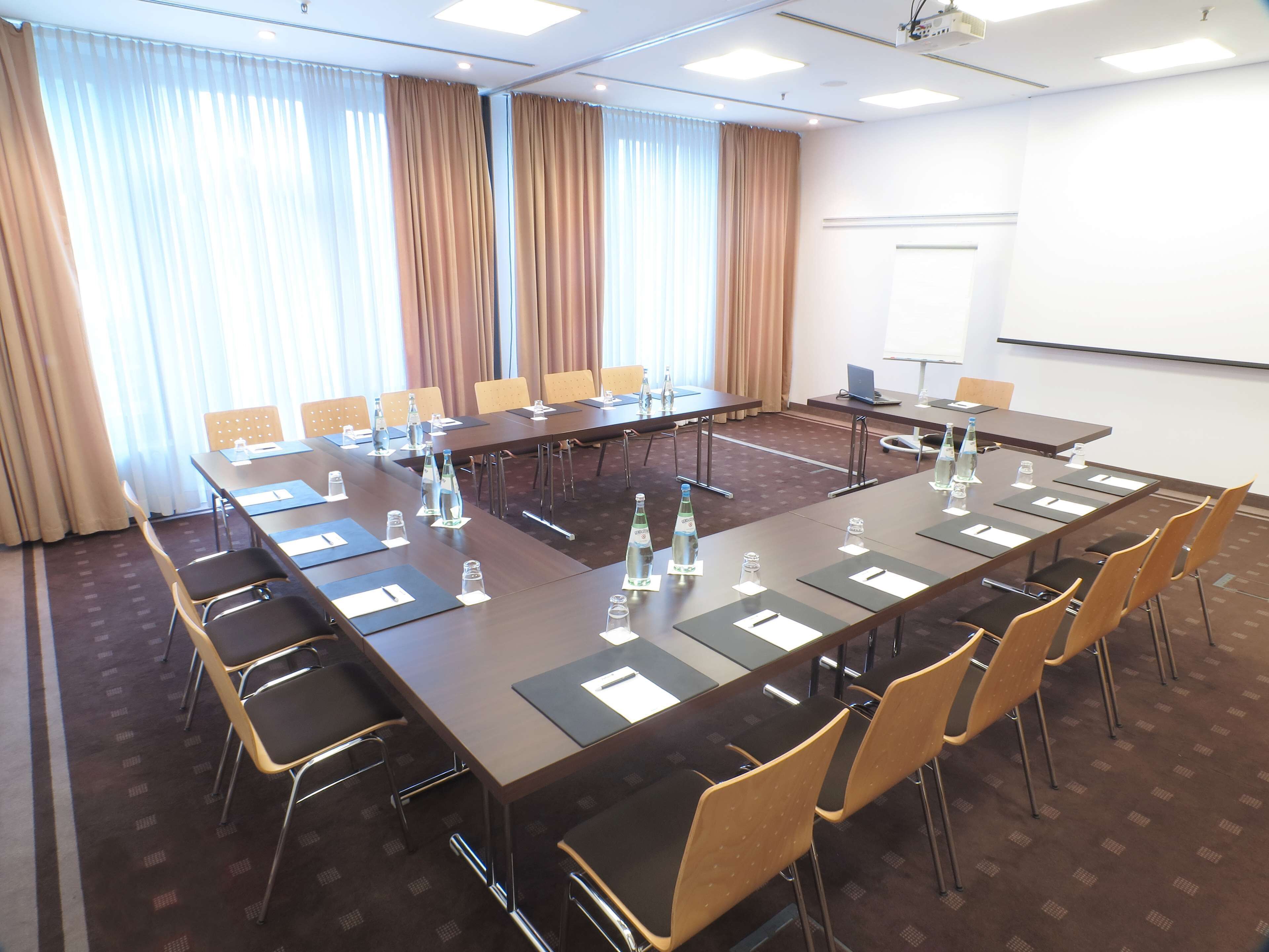 A conference room with a long table, chairs, water bottles, and a projector screen.