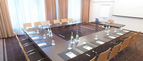A conference room with a long table, chairs, water bottles, and a projector screen.