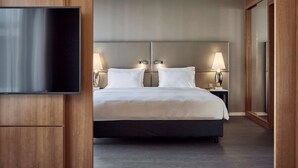 Una habitación de hotel moderna con una cama grande, dos lámparas de noche, un televisor de pantalla plana montado en un panel de madera y un espejo grande en la pared.