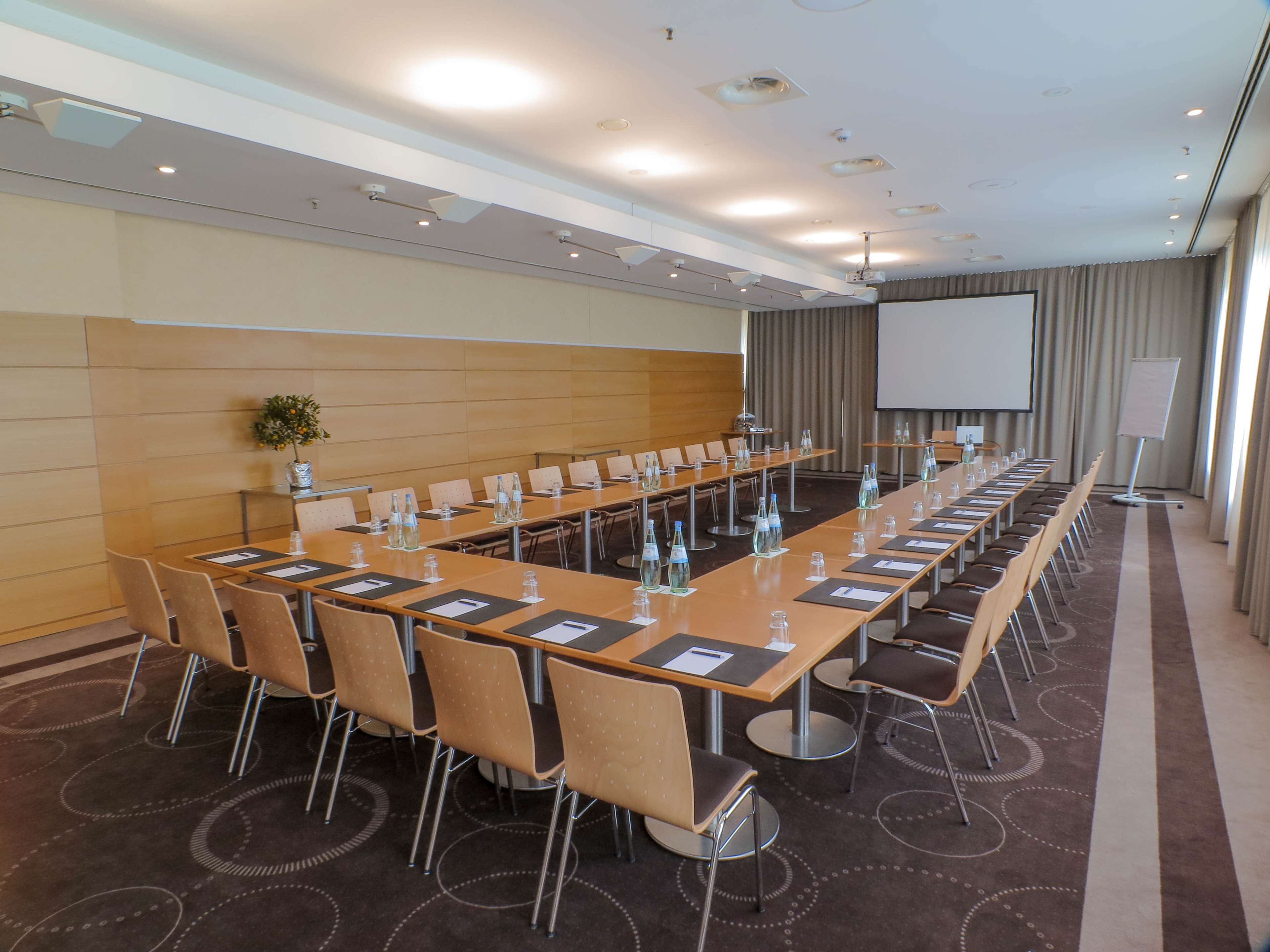 A conference room with a long table, chairs, water bottles, and a projector screen.