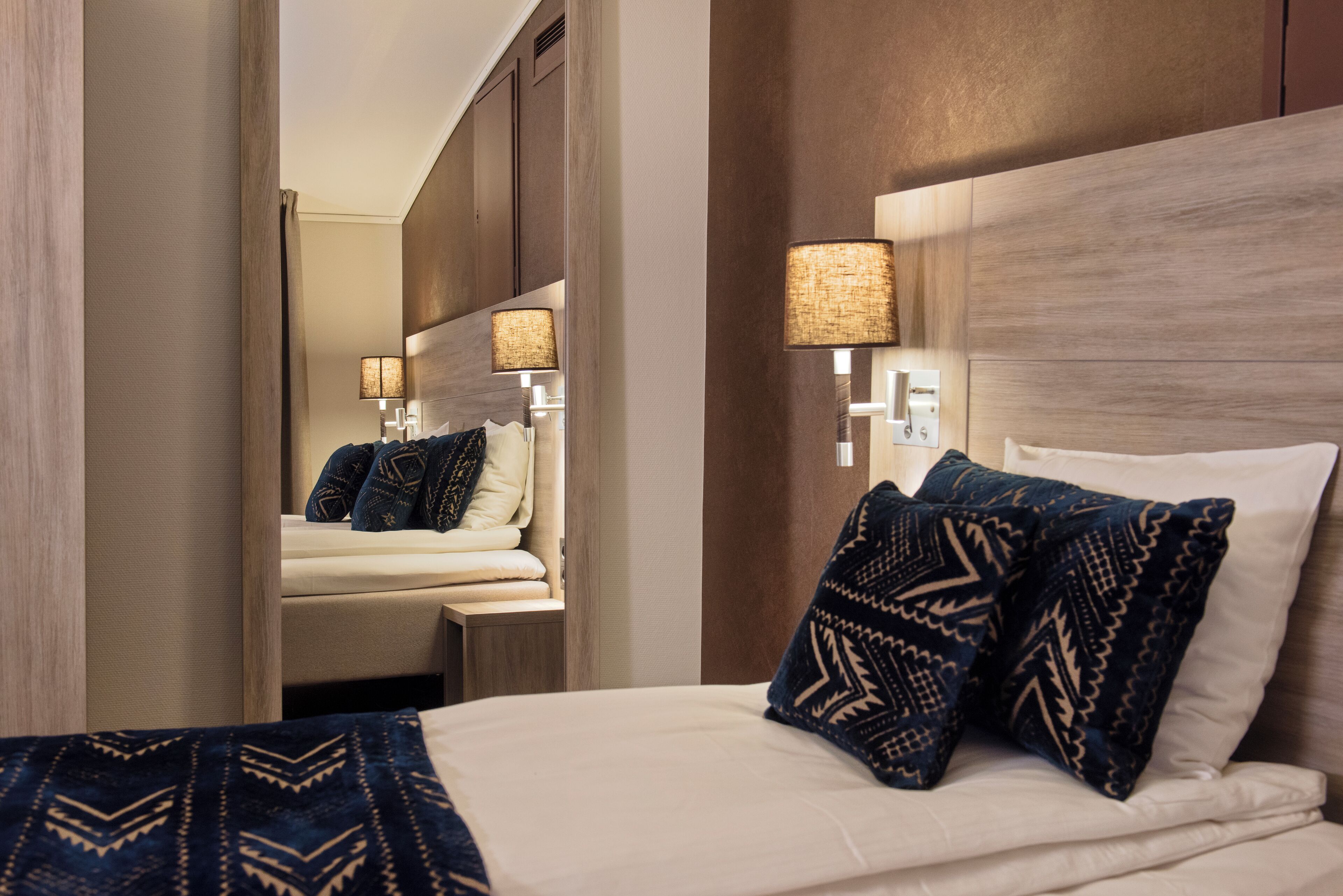Una habitació d'hotel amb un llit gran, dues làmpades de nit i un mirall que reflecteix l'habitació.