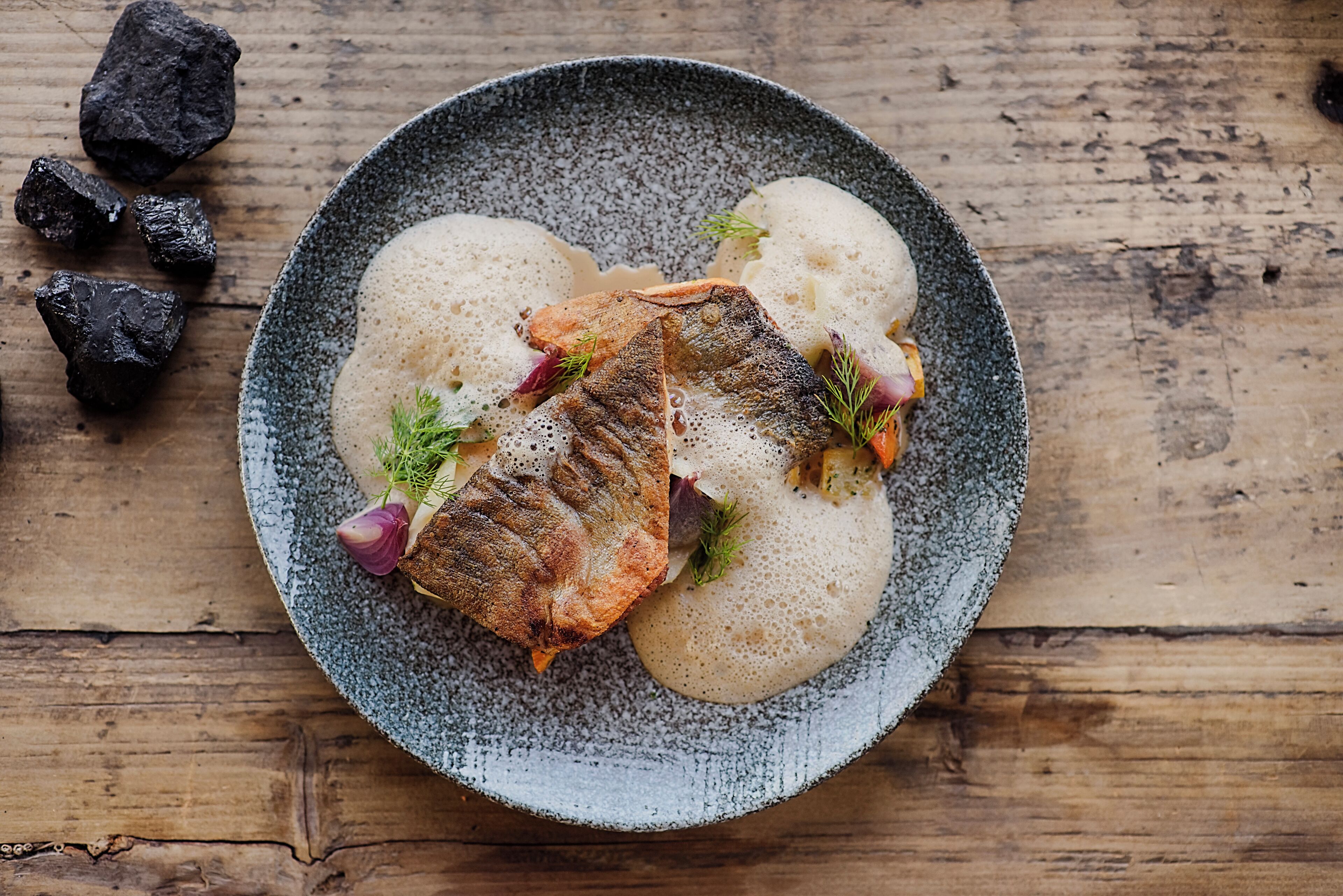 Ein Teller mit Fisch, Kartoffeln und Gemüse auf einem rustikalen Holztisch.