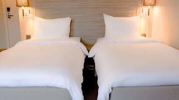 A hotel room with two beds, each with white bedding and headboards, and bedside lamps.
