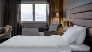 A hotel room with a bed, a desk, a chair, a lamp, and a view of a mountain through the window. - Radisson Blu Polar Hotel Spitsbergen (Longyearbyen)
