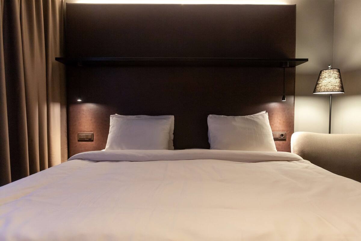 A hotel room with a large bed, a headboard, bedside lamps, and a wall-mounted light fixture.