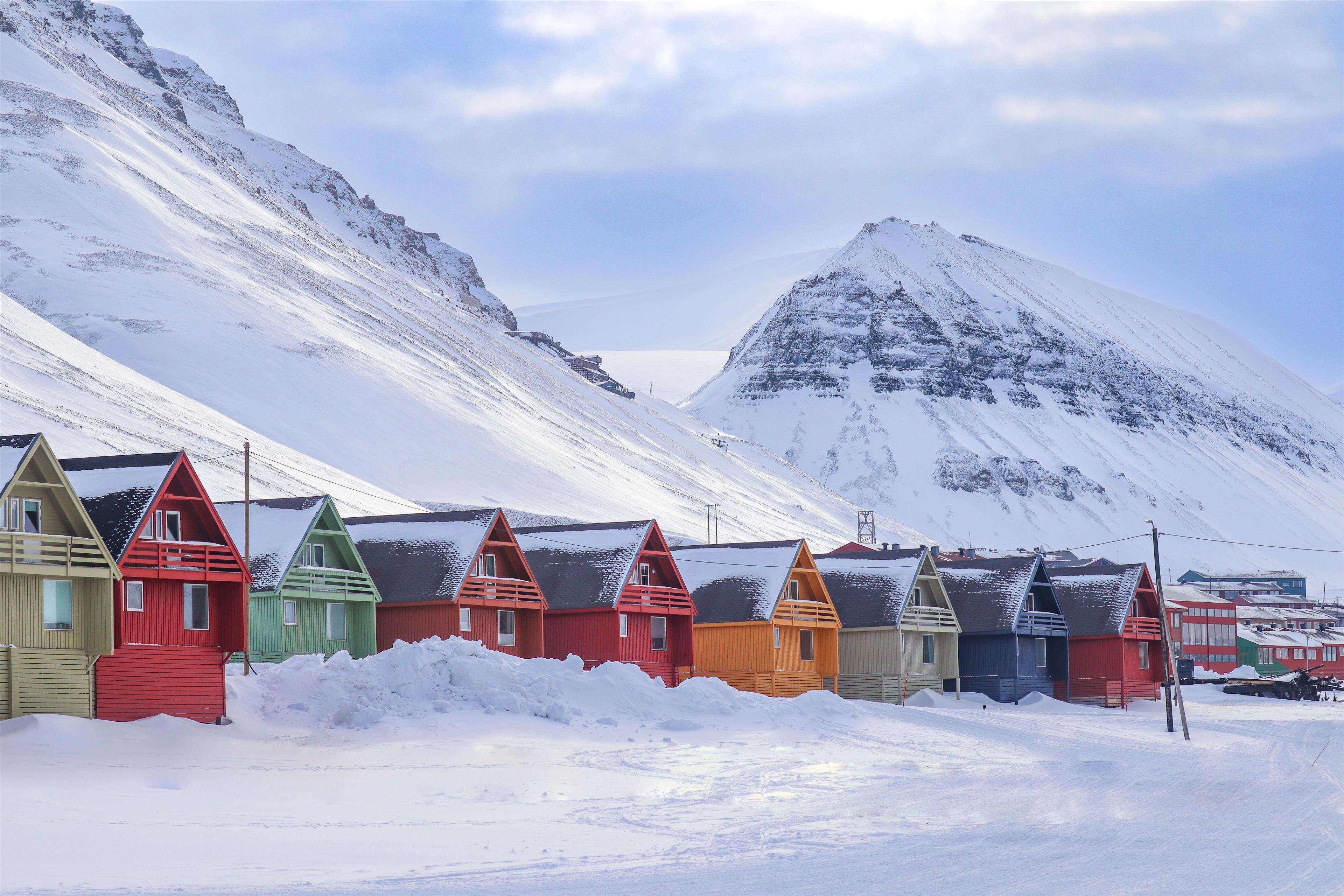 A row of colorful houses in a snowy landscape with a mountain in the background.