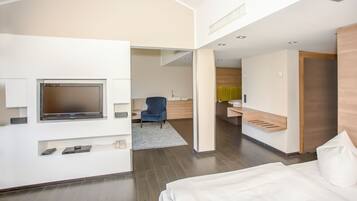 A modern hotel room with a flat-screen TV, a blue chair, a wooden desk, and a bed.