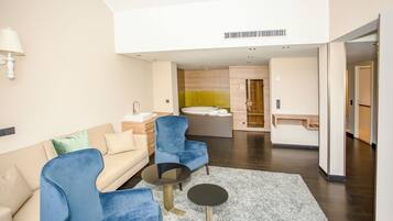 Ein modernes Hotelzimmer mit einer Couch, zwei Sesseln, einem kleinen runden Tisch, einem Badezimmer mit einer Badewanne und einem Flur, der zu einem weiteren Zimmer führt.