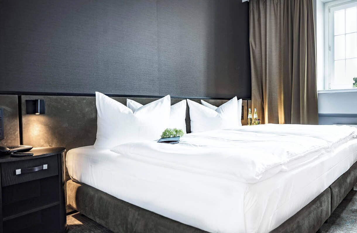 Une chambre d’hôtel avec un grand lit, une table de chevet avec une lampe et une fenêtre avec des rideaux.