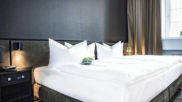 Ein Hotelzimmer mit einem großen Bett, einem Nachttisch mit Lampe und einem Fenster mit Vorhängen.