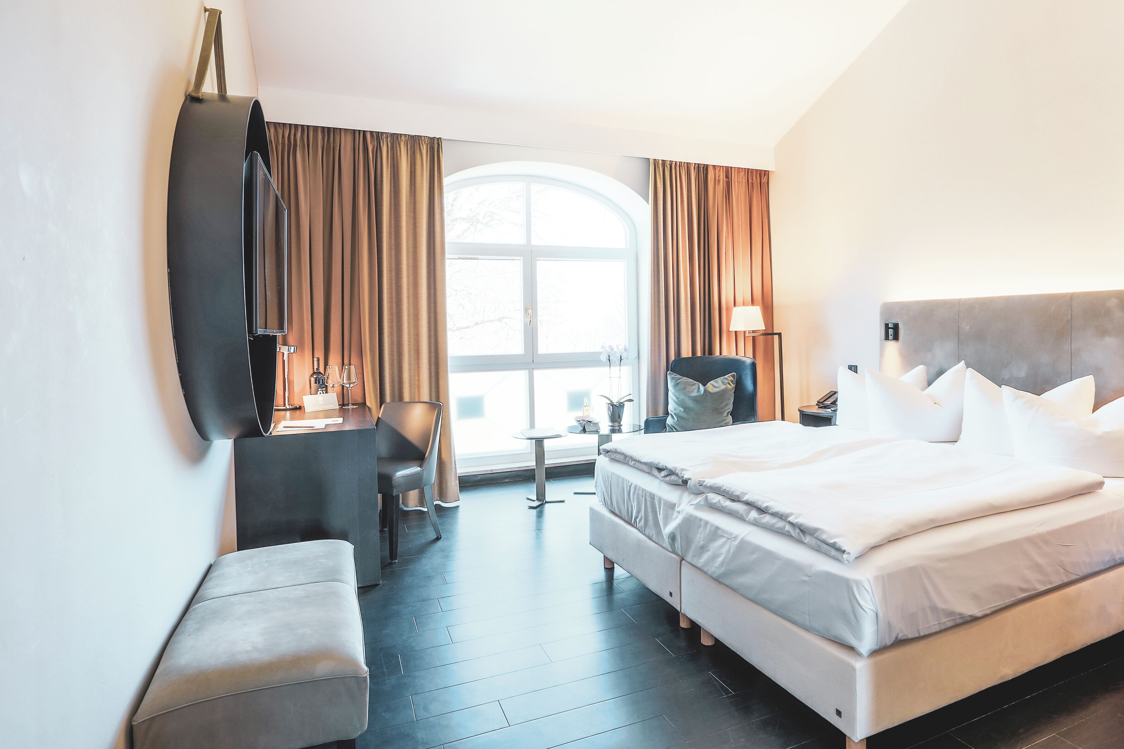 A hotel room with a large bed, a desk, a chair, a small table, and a window with curtains.