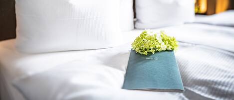 A neatly made bed with white linens and pillows, a blue book, and a small bouquet of flowers.