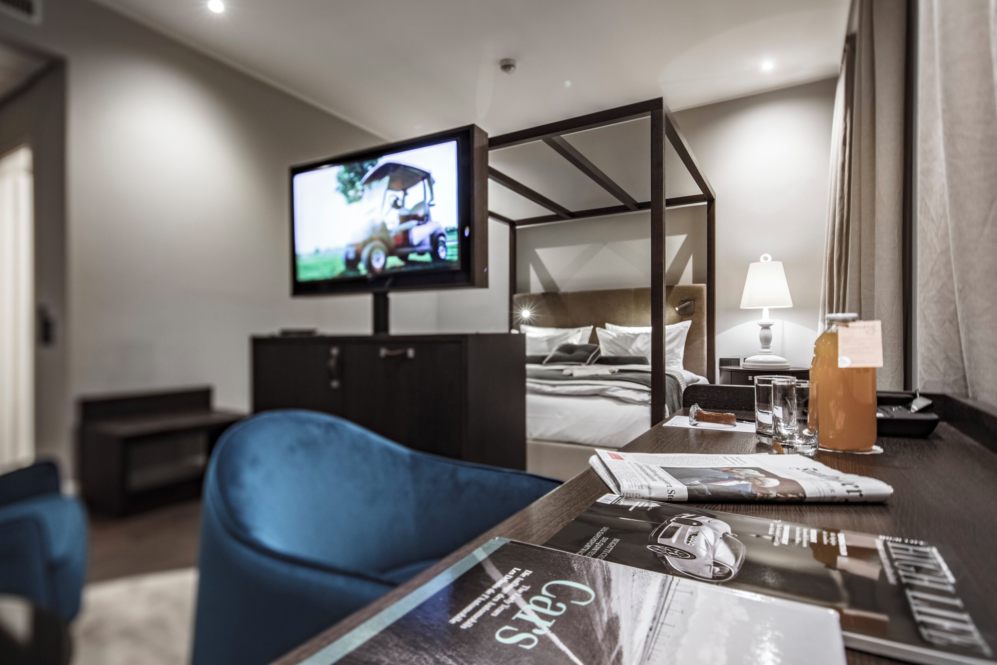 Ein Hotelzimmer mit Bett, Schreibtisch mit Lampe, Fernseher an der Wand und einem Sessel.