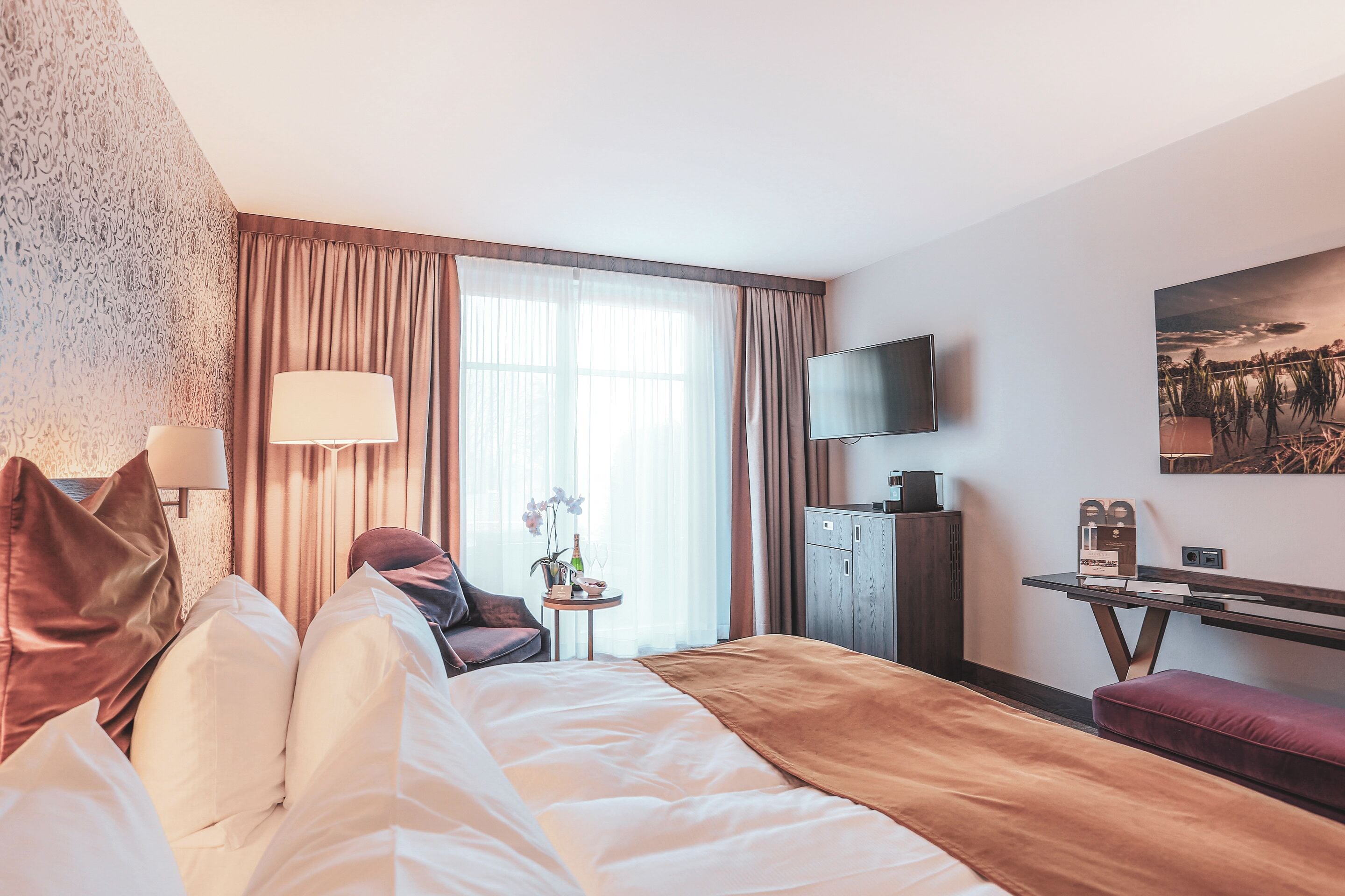 Una camera d'albergo con un letto, una scrivania, una televisione e una finestra con tende.