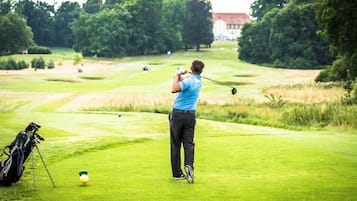 Golfers can tee off on the lush green course, surrounded by mature trees and a picturesque clubhouse.
