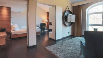 A modern hotel room with a bed, a desk, a chair, a large mirror, and a view of the outdoors.