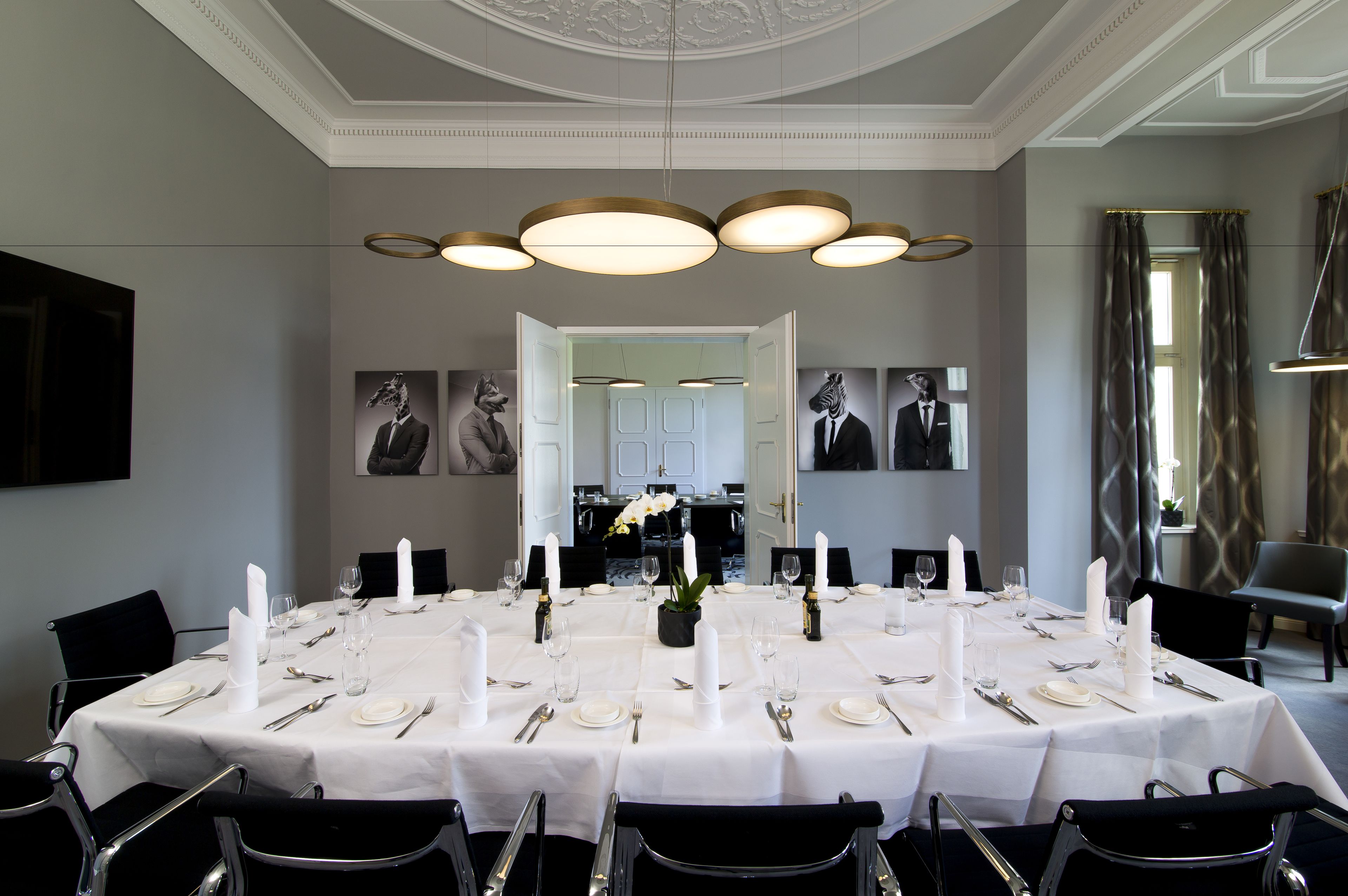 A formal dining room with a long table set for a meal, elegant lighting fixtures, and framed artwork on the walls.