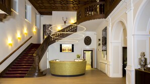 Een statige lobby met een wenteltrap, een receptiebalie en een hoog plafond met versierde houtsnijwerken.
