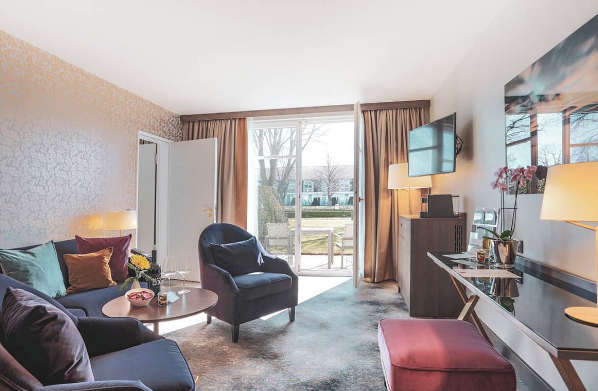 A hotel room with a sofa, armchair, coffee table, and a TV mounted on the wall.