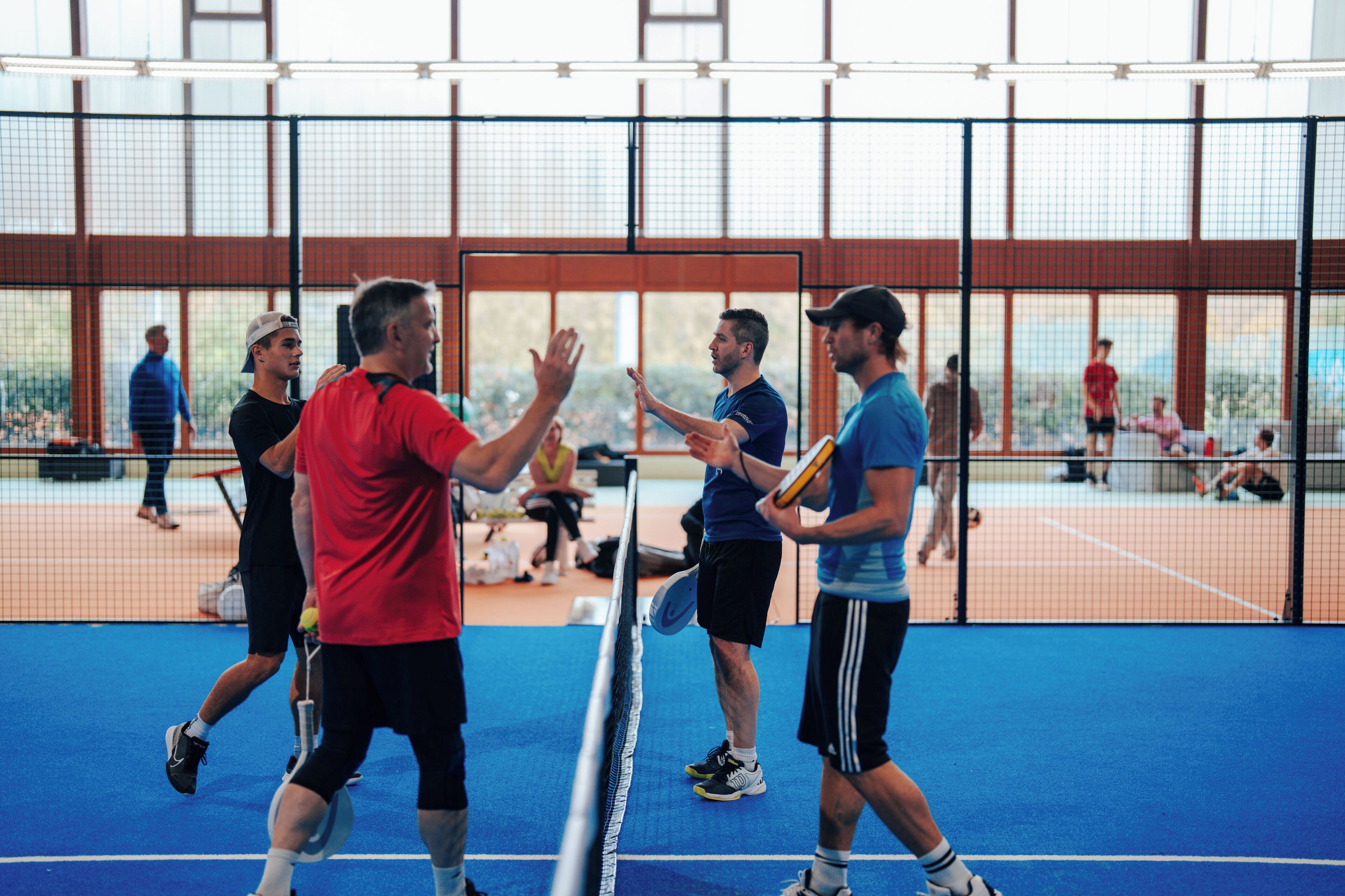 Ein Tennisplatz mit Spielern in roten und blauen Shirts.