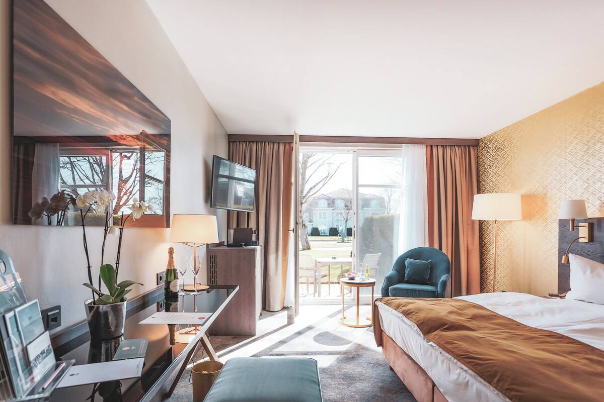 A hotel room with a bed, desk, chair, and a view of the outdoors.