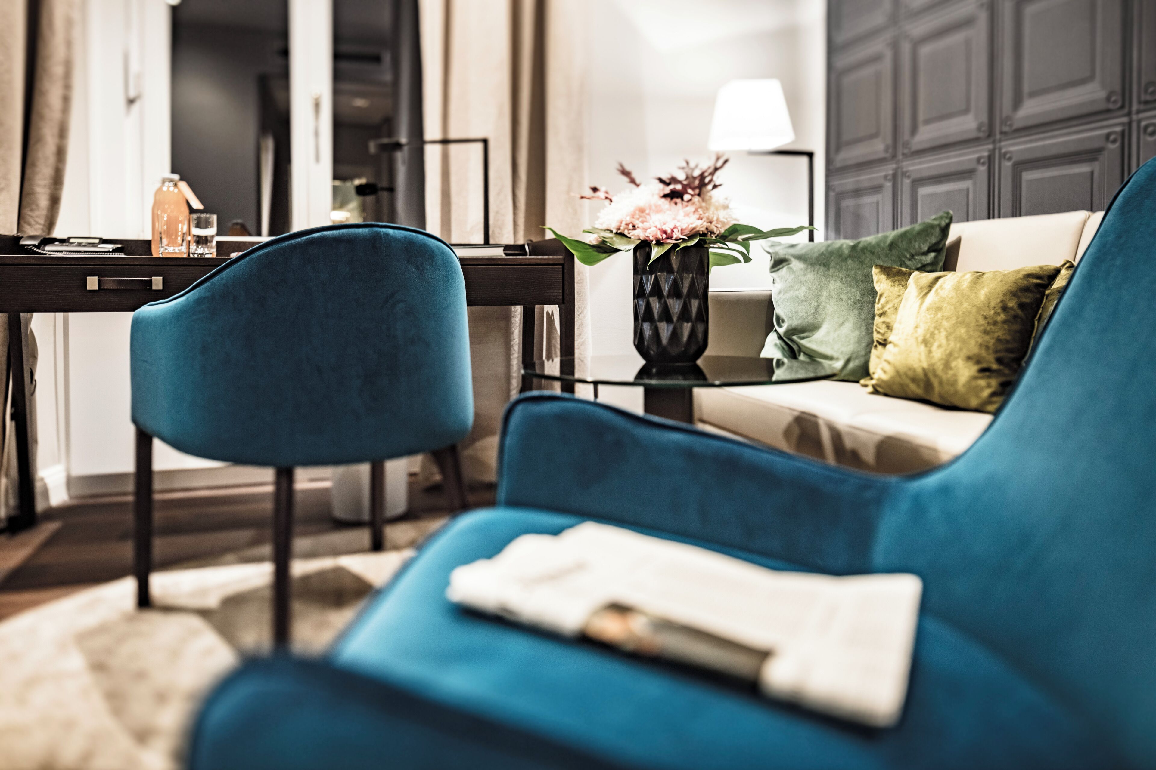 Een moderne woonkamer met een blauwe bank, een bijzettafeltje, een vaas met bloemen en een lamp.
